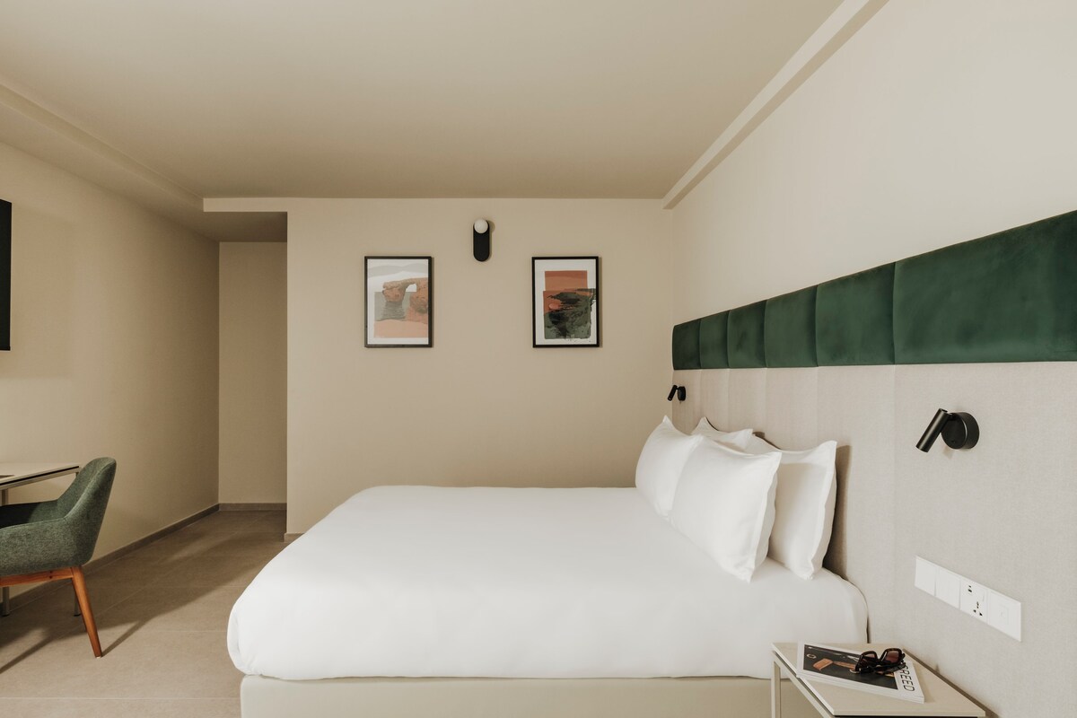 Habitación de hotel con una cama, un escritorio, una silla y dos cuadros en la pared.