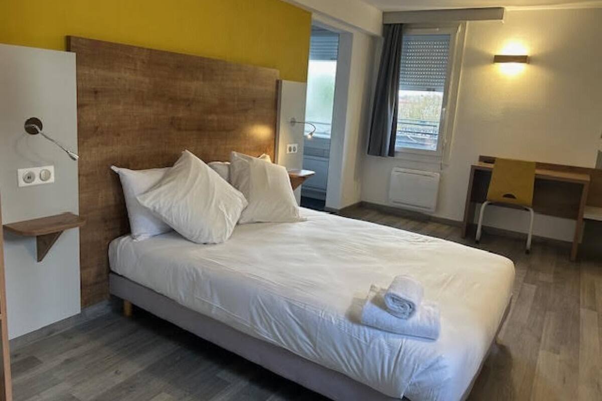 Una habitación de hotel con una cama, cabecera de madera, un escritorio y una silla.