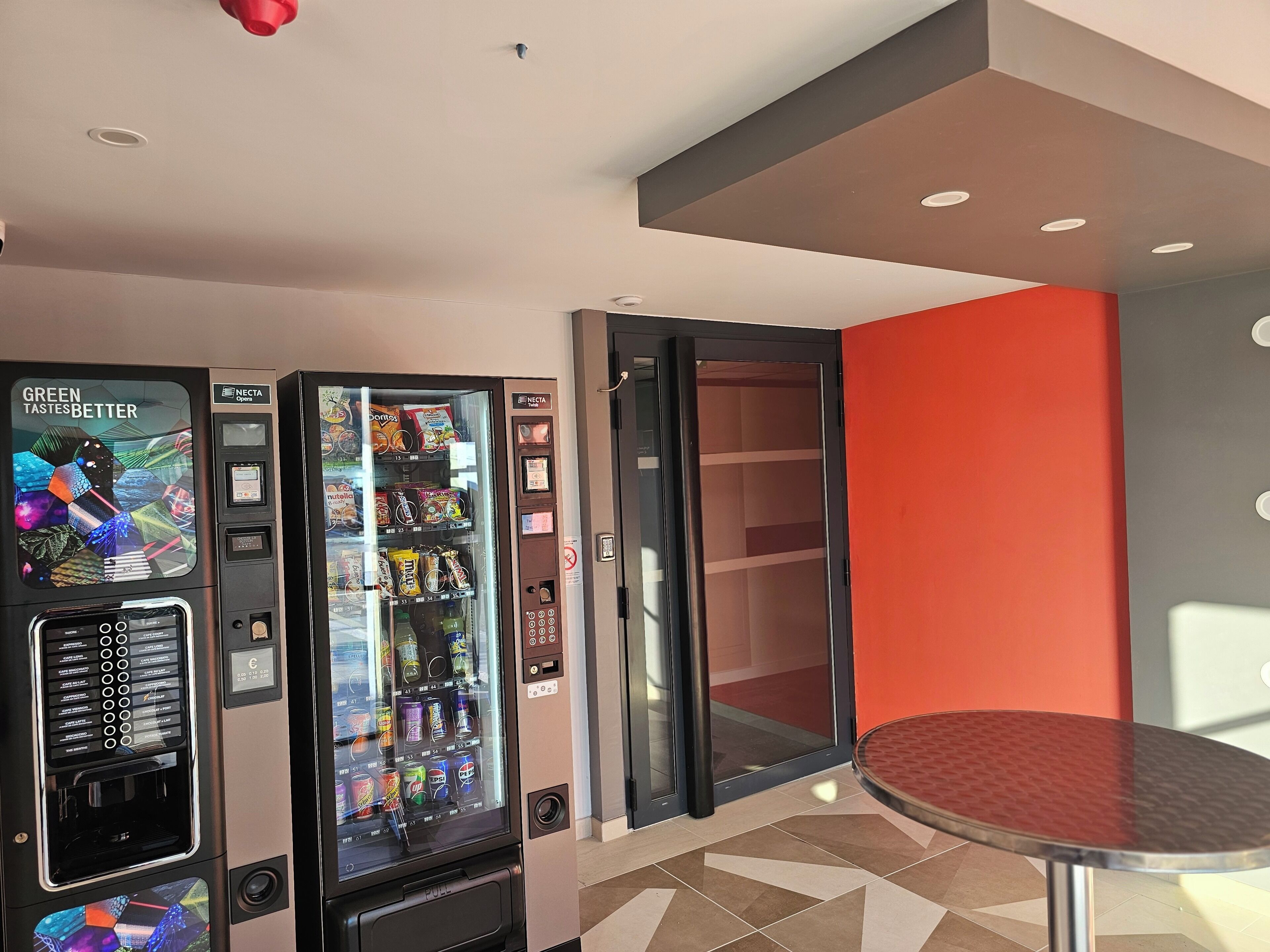 A vending machine with a variety of snacks and drinks, a glass door, and a small table with a red surface.