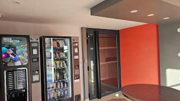 A vending machine with a variety of snacks and drinks, a glass door, and a small table with a red surface.