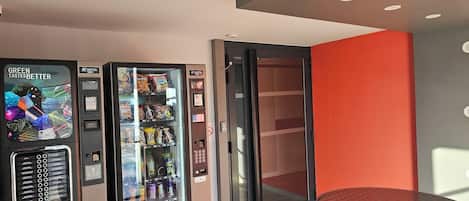 A vending machine with a variety of snacks and drinks, a glass door, and a small table with a red surface.