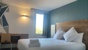 A hotel room with a large bed, a desk, and a window with curtains.