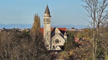Une église dotée d’un haut clocher et d’un toit rouge, entourée d’arbres et de maisons dans une région vallonnée.