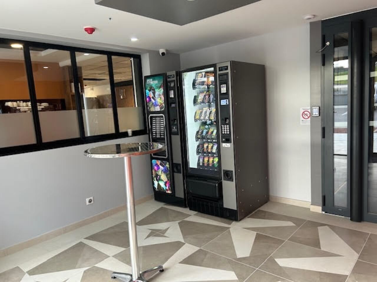 A modern interior with vending machines, a glass partition, and a metal table.