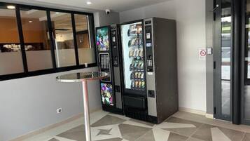 A modern interior with vending machines, a glass partition, and a metal table.