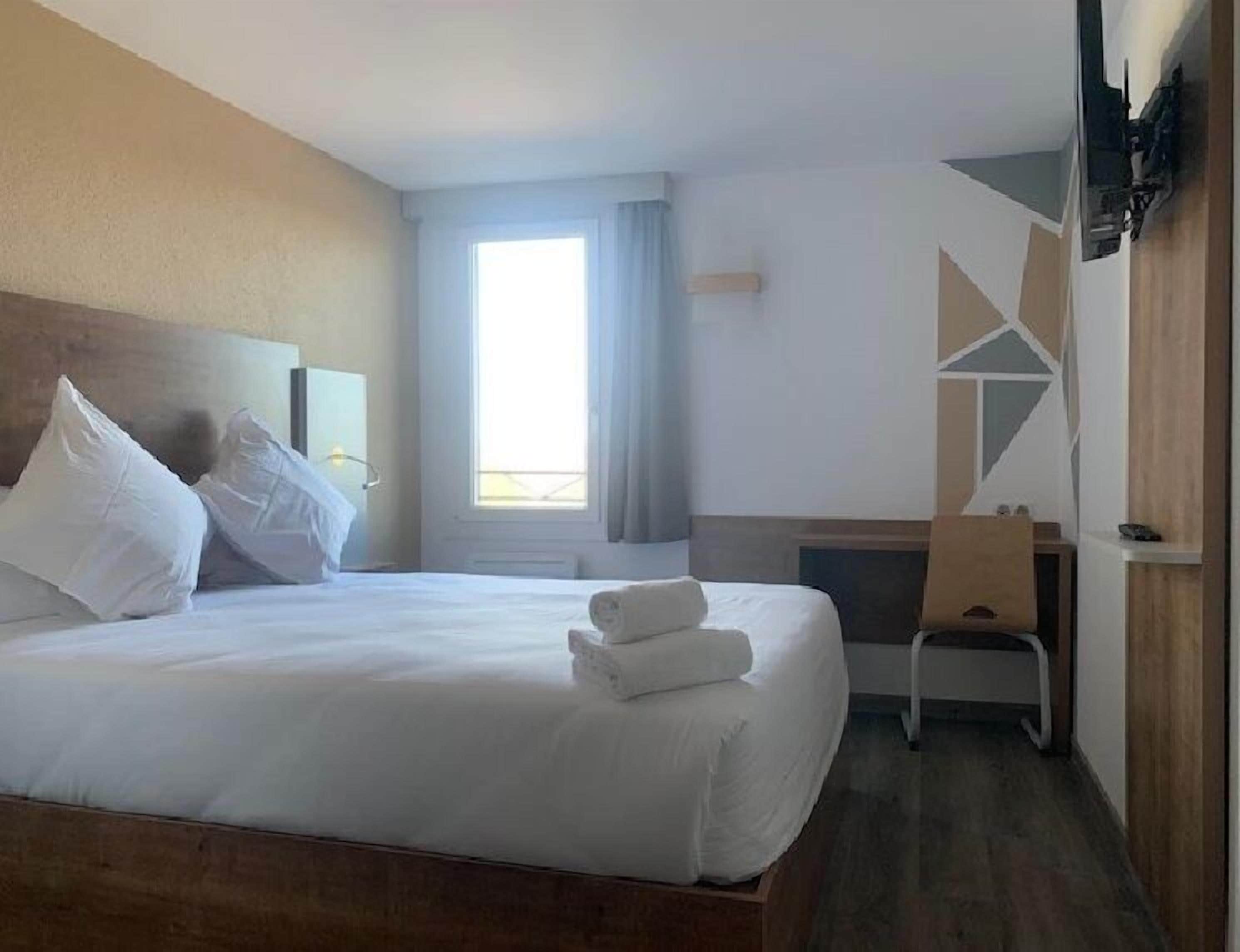 A hotel room with a bed, a desk, and a chair.