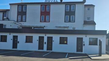 A hotel with a white facade, multiple doors, and a parking lot in front.