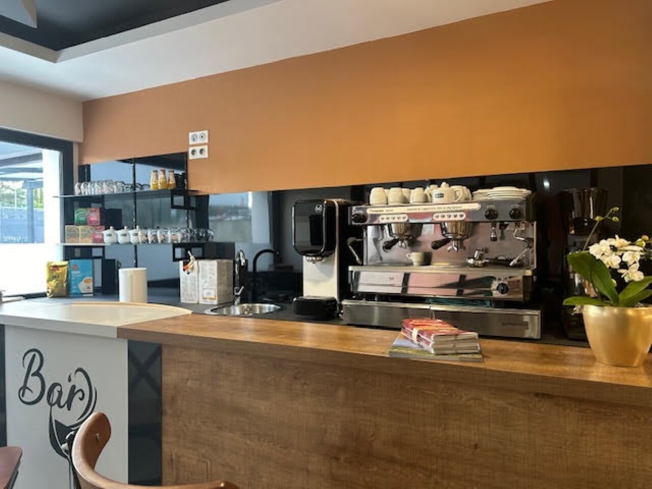 A modern bar area with a coffee machine, shelves with cups and condiments, and a sign that reads "Bar".