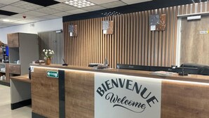 A reception desk with a 'BIENVENUE Welcome' sign, a clock, and a 'Local Tour' sign.