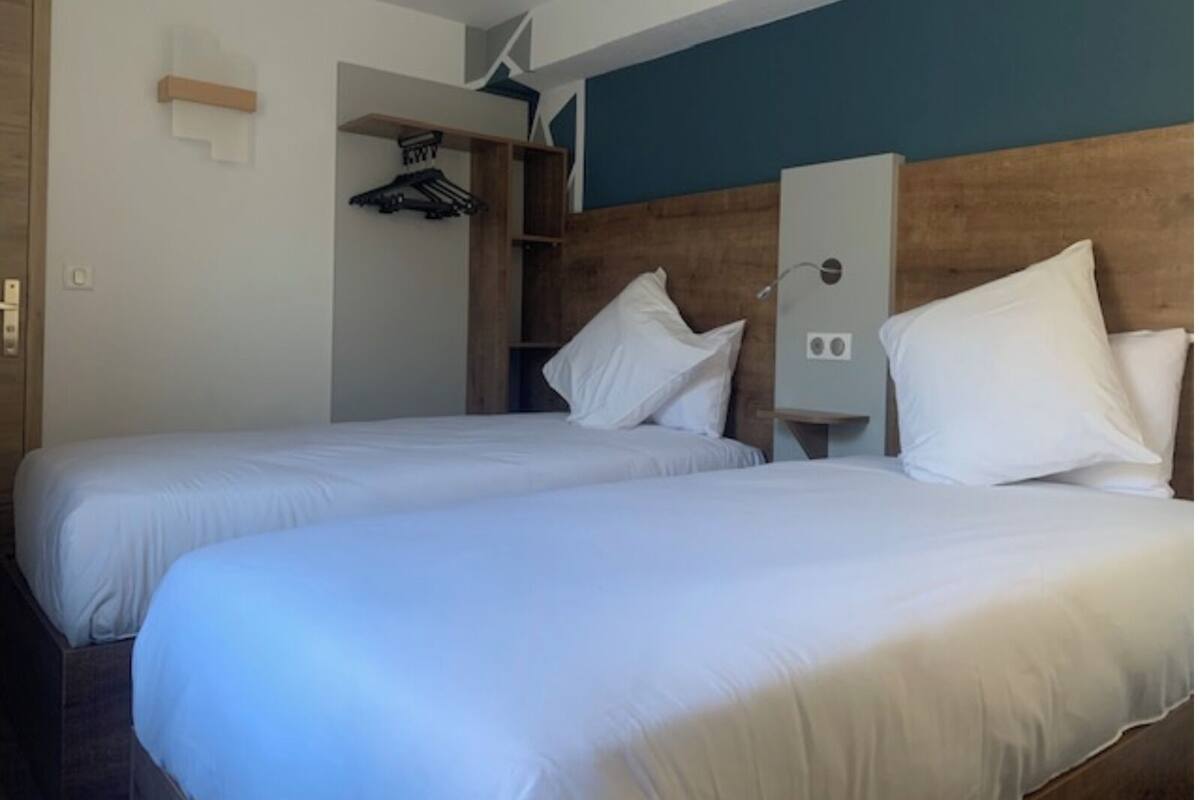 Una habitación de hotel con dos camas, cabecero de madera, un armario y una pequeña estantería.