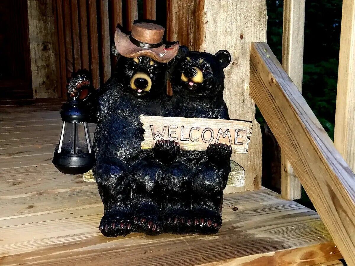 Um deck de madeira com uma escultura de urso negro segurando um letreiro com a palavra 'WELCOME'.