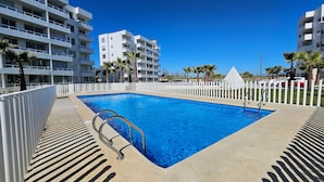 A rectangular swimming pool with a white fence, surrounded by buildings and palm trees. - Oceana Suites Distrito Verde (La Serena)
