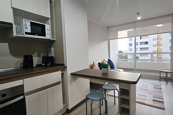 A modern kitchen with a microwave, coffee maker, and a dining area with a table and two chairs. - Oceana Suites Distrito Verde (La Serena)