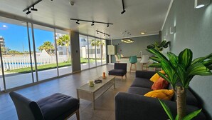 A modern interior with a sofa, chairs, a coffee table, and a large window offering a view of palm trees and buildings. - Oceana Suites Distrito Verde (La Serena)