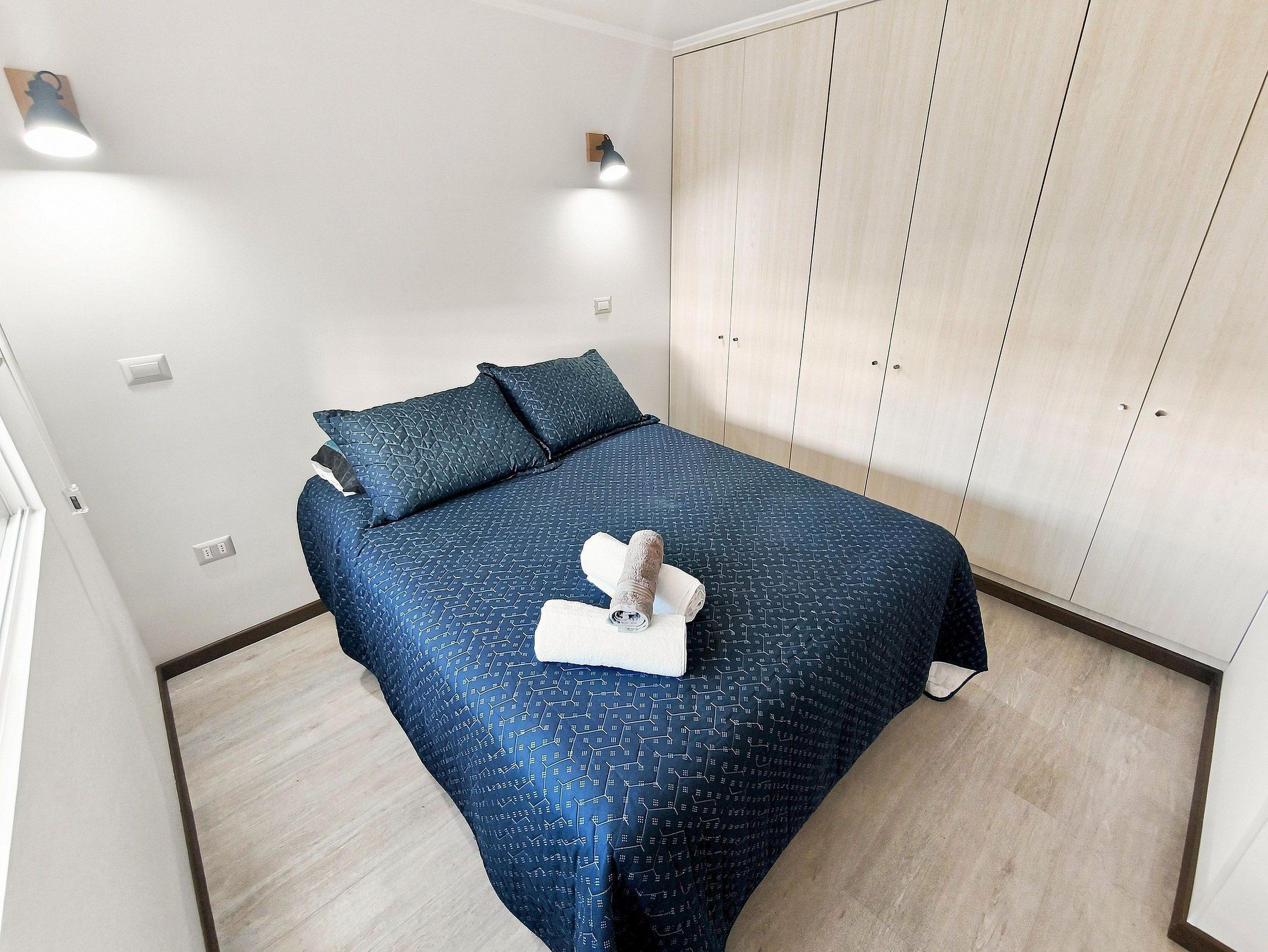 Un dormitorio con cama, almohadas, una lámpara de noche, un armario y una toalla sobre la cama.