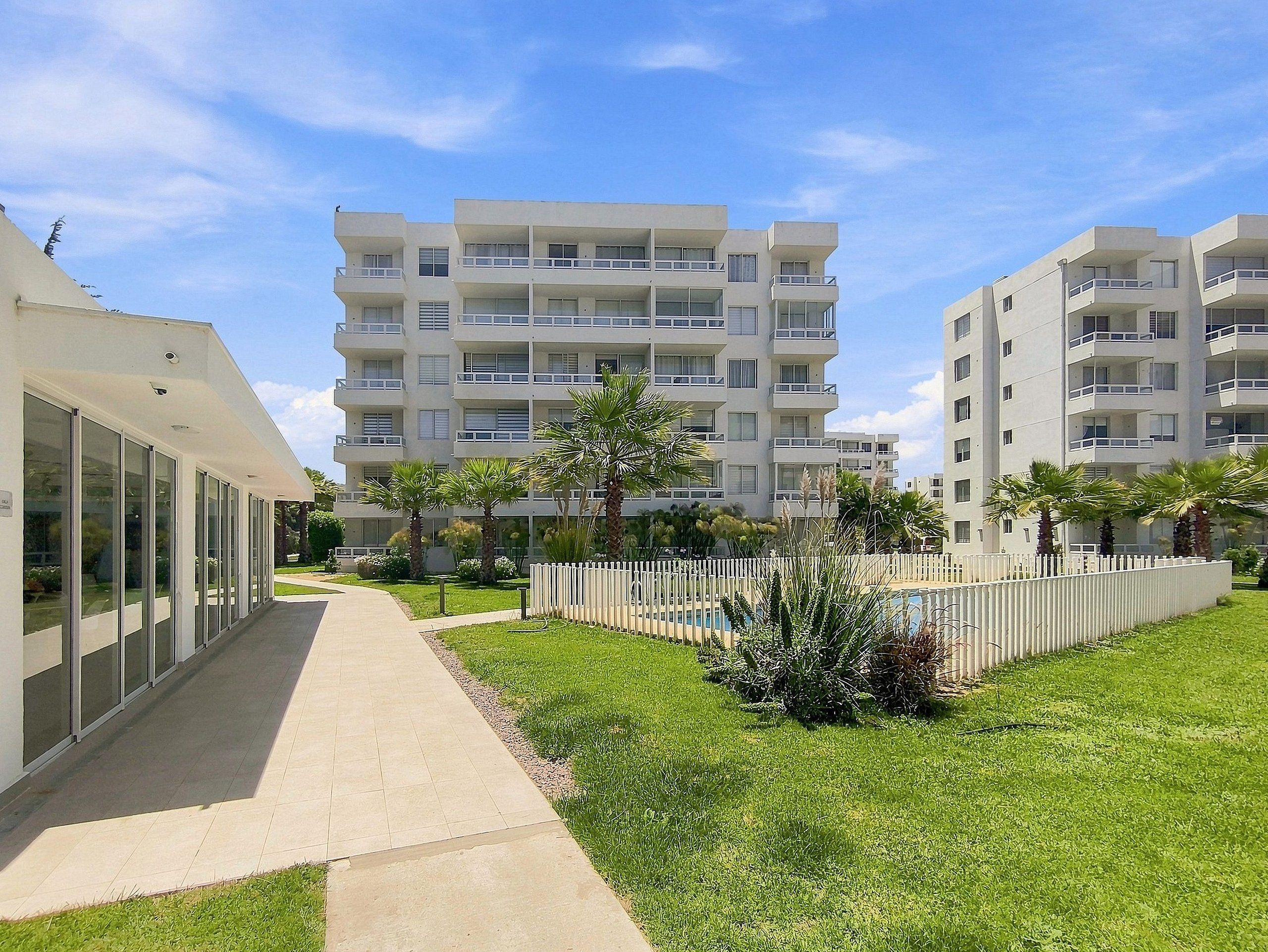 A modern apartment building with multiple balconies, a paved walkway, and well-maintained greenery.