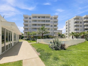Um edifício de apartamentos moderno com várias varandas, um caminho pavimentado e vegetação bem cuidada.