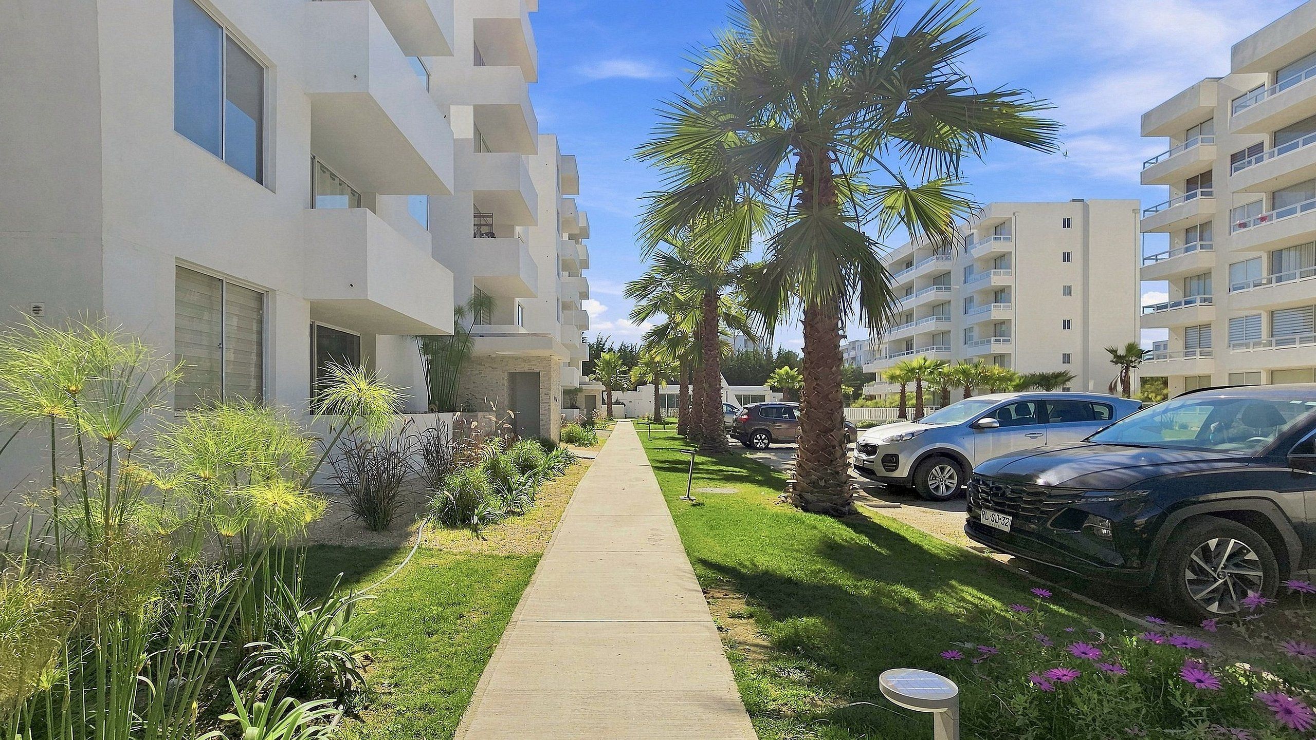 A residential building with a central pathway, parked cars, and a clear sky.
