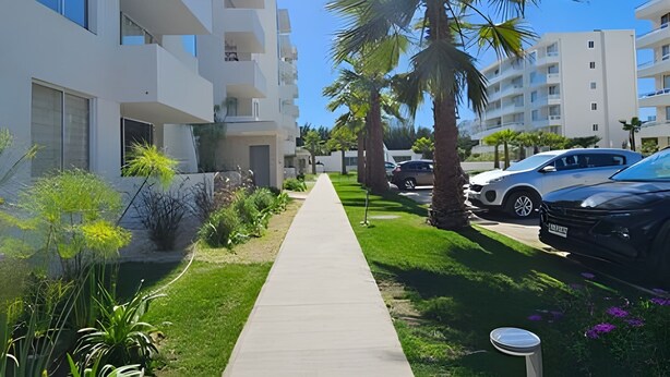 A modern residential building with a central pathway, parked cars, and lush greenery. - Oceana Suites Distrito Verde (La Serena)