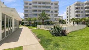 A modern apartment building with multiple balconies, a paved walkway, and well-maintained greenery. - Oceana Suites Distrito Verde (La Serena)