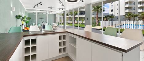 A modern kitchen with a built-in island, a dining area with chairs, and a view of a swimming pool and buildings outside.