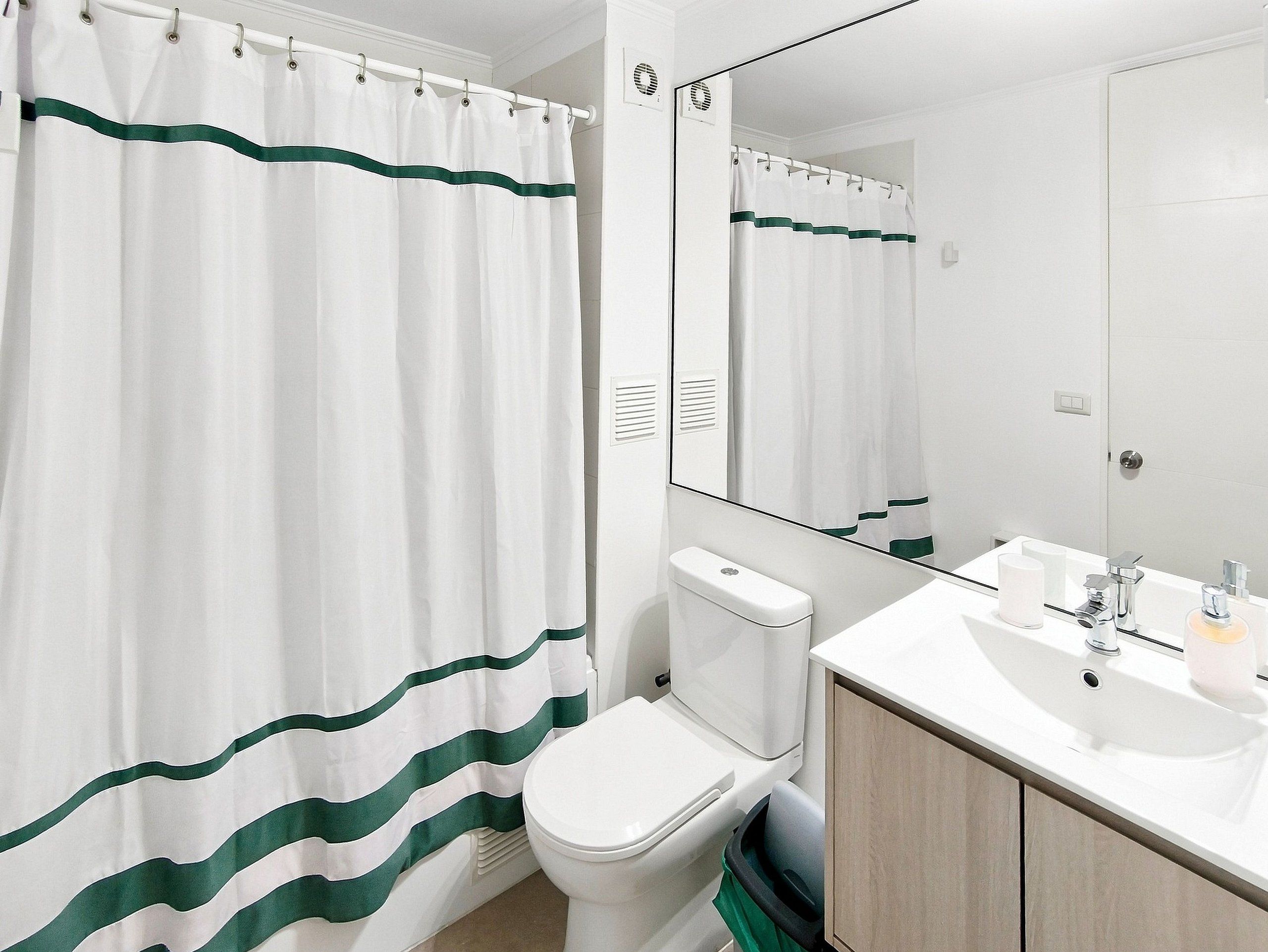 A bathroom with a white toilet, a sink with a mirror, and a shower curtain with green stripes.