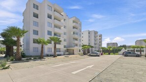 A multi-story residential building with a flat facade, several balconies, and a parking area with cars. - Oceana Suites Distrito Verde (La Serena)