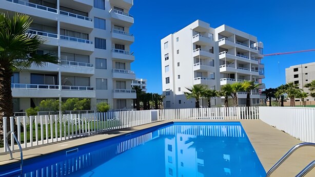 A swimming pool with a white fence, surrounded by modern multi-story buildings. - Oceana Suites Distrito Verde (La Serena)