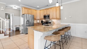 Una cocina moderna con armarios de madera, electrodomésticos de acero inoxidable, encimera de granito y taburetes de bar.