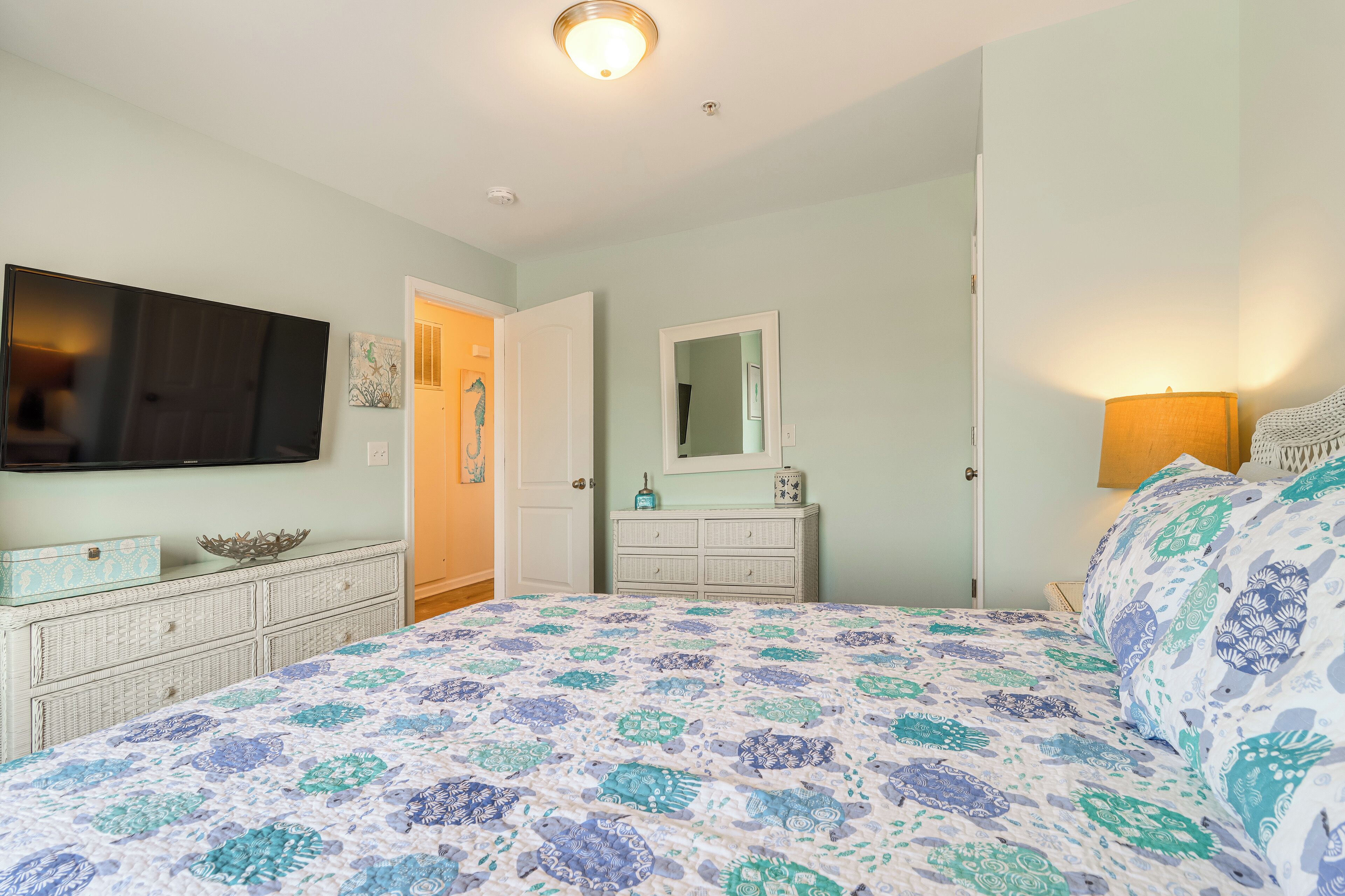 A bedroom with a bed, dresser, television, and a door leading to another room.