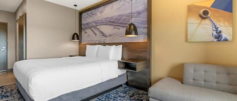 Una habitación de hotel moderna con una cama grande, una zona de estar, una obra de arte en la pared y una lámpara colgante.