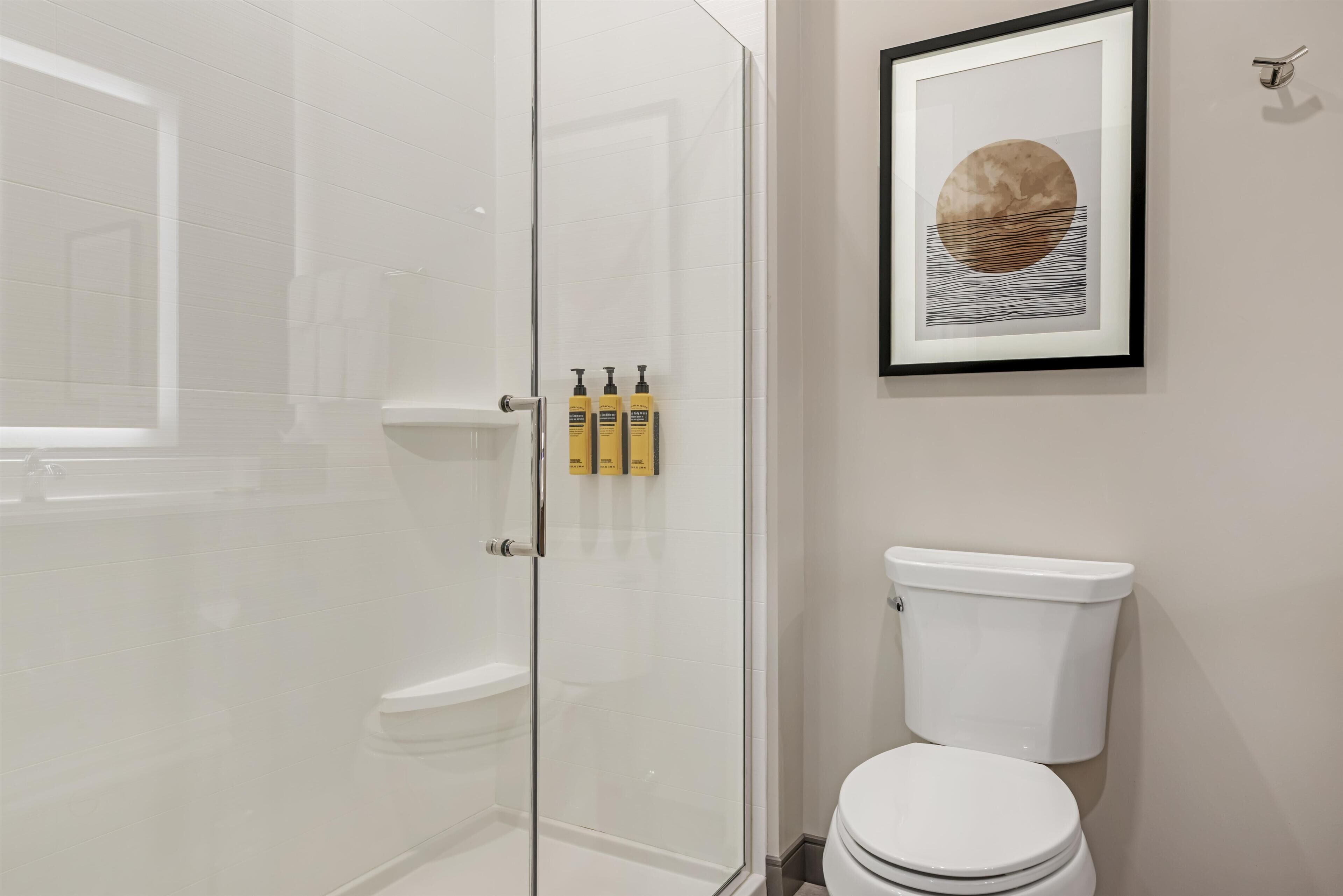 A bathroom with a glass shower enclosure, a toilet, and a framed artwork on the wall.