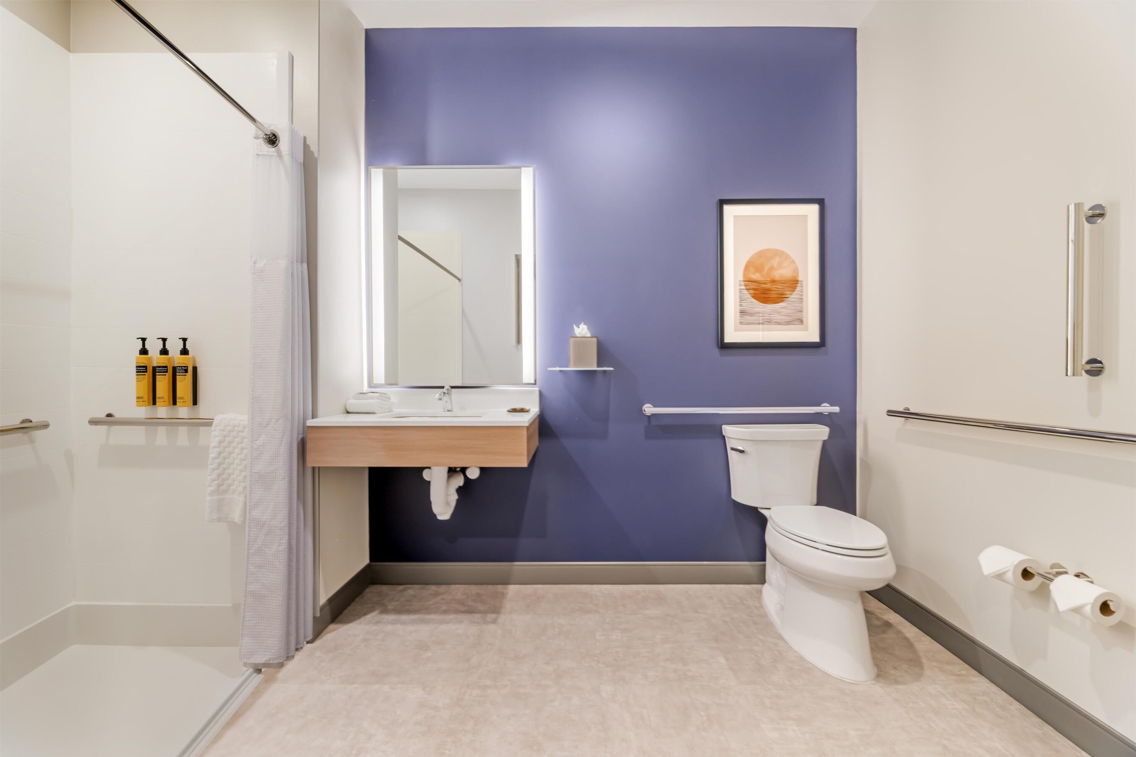 A modern bathroom with a shower, toilet, sink, and a framed artwork on the wall.