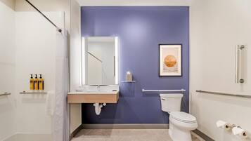 A modern bathroom with a shower, toilet, sink, and a framed artwork on the wall.