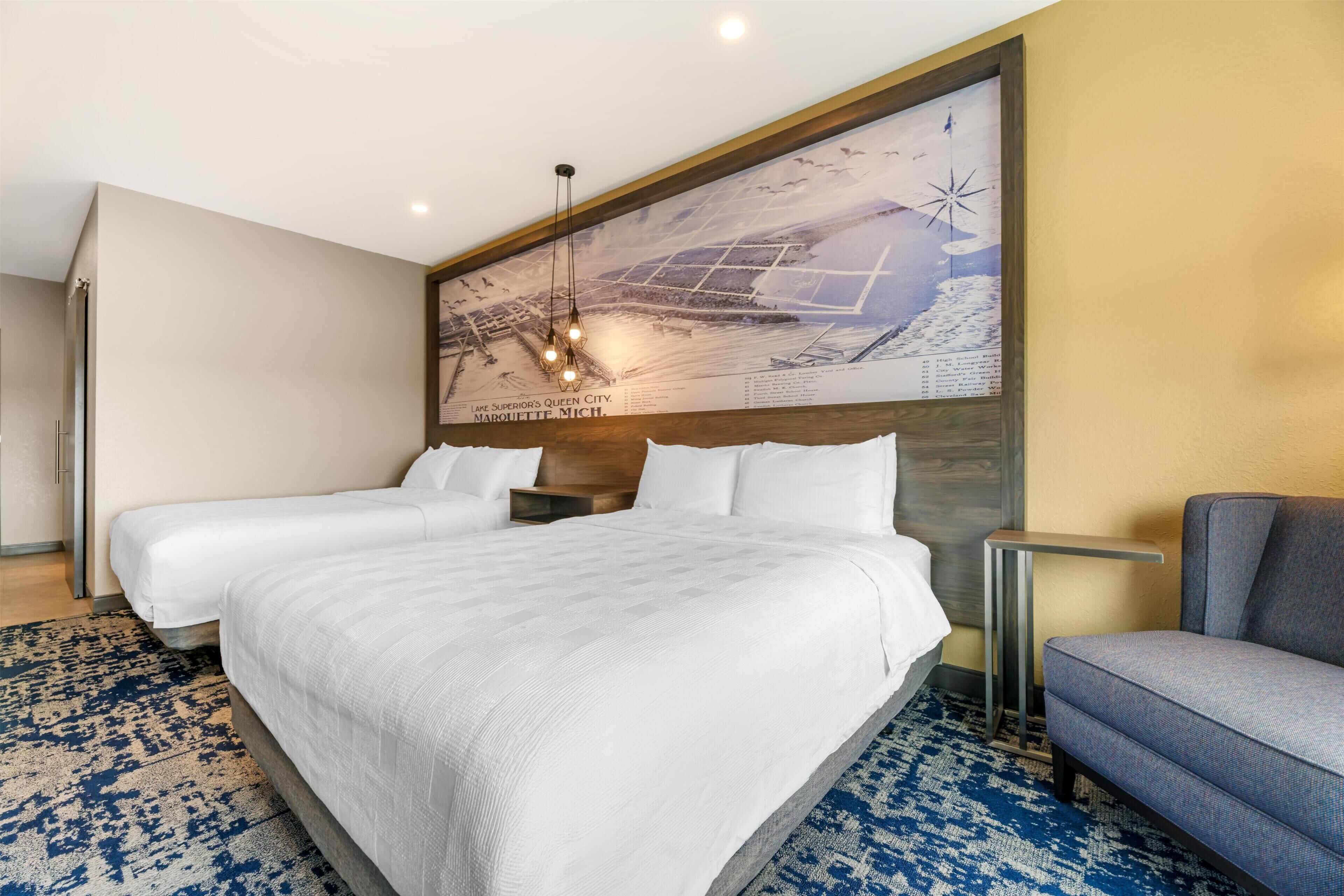 A hotel room with a large bed, two bedside tables, a chair, a large wall map, and a patterned rug.
