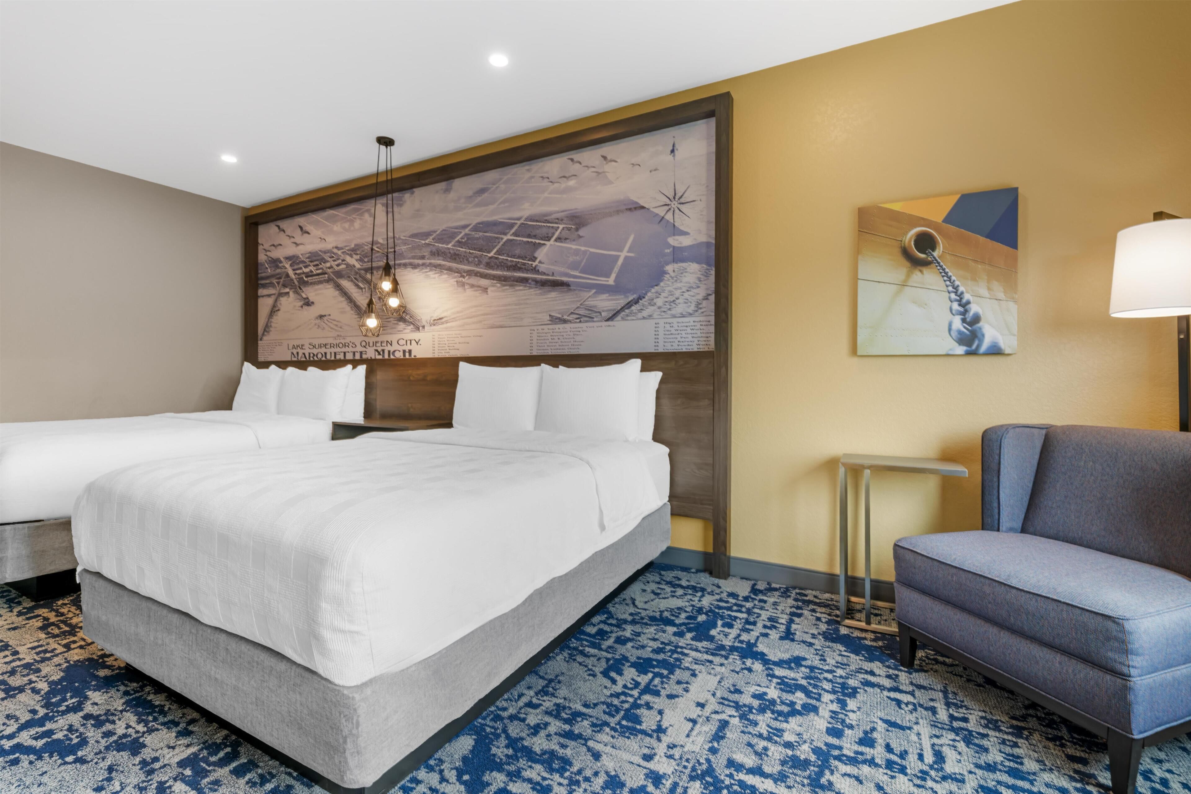 Habitación de hotel con una cama grande, dos mesitas de noche, una silla, una obra de arte en la pared y una alfombra estampada.