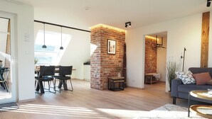 Un salon moderne avec un mur d’accent en briques, un coin repas baigné de lumière naturelle et un espace détente confortable avec un canapé gris.