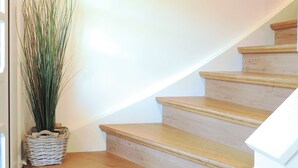 Un escalier en bois, agrémenté d’une plante en pot et d’un tableau encadré représentant un cerf, est accroché au mur.