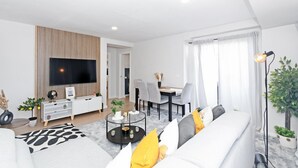 Ein modernes Wohnzimmer mit Flachbildfernseher, Essbereich mit Tisch und Stühlen und einer Couch mit Kissen.