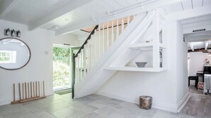 Ein geräumiges Zimmer mit einer weißen Treppe, einem runden Spiegel und einem kleinen Holzschemel.
