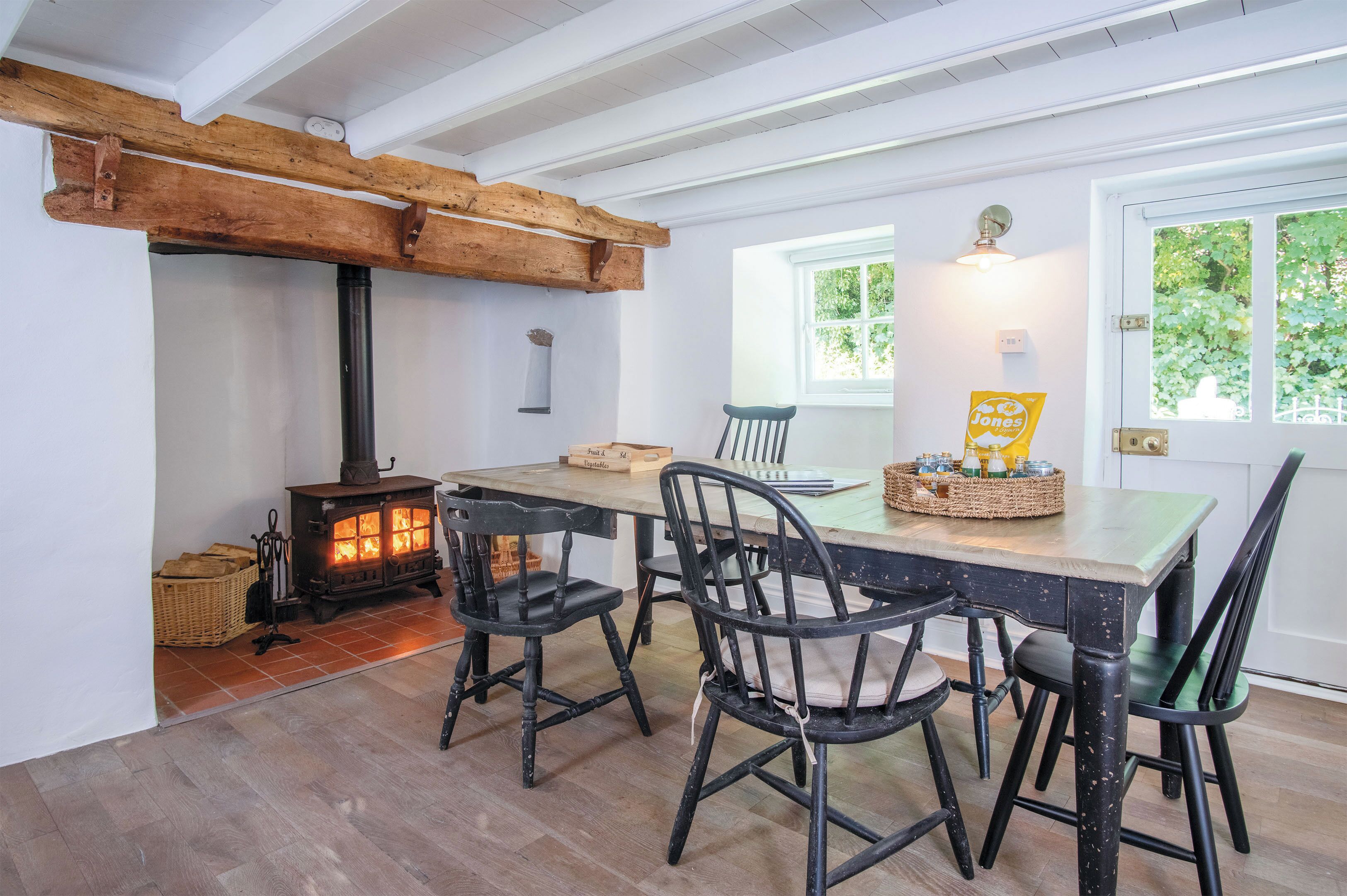 A dining area with a wooden table, four chairs, a stove, and a window with a view of greenery.