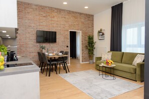 Un espacio de estar moderno con pared de ladrillo, televisor de pantalla plana, zona de comedor, sofá verde y área de cocina.