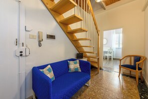 Una habitación con un sofá azul, una escalera de madera y una silla.