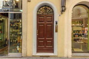 Una puerta marrón con un arco blanco encima, un cartel con el número 15 a la derecha, y una tienda con ventanas de vidrio a la izquierda.