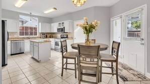 Eine moderne Küche mit weißen Schränken, einer zentralen Kochinsel und einem Essbereich mit Tisch und Stühlen.