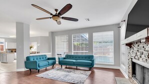 Ein geräumiges Wohnzimmer mit großem Fenster, Kamin und Deckenventilator.
