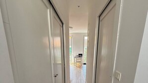 Un corridoio stretto con pavimento in legno e pareti bianche, che conduce a una zona con balcone, tavolo e sedie.