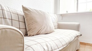 Een beige bank met een geruit patroon, geplaatst tegen een witte muur met een raam.