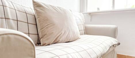 A beige sofa with a checkered pattern, positioned against a white wall with a window.