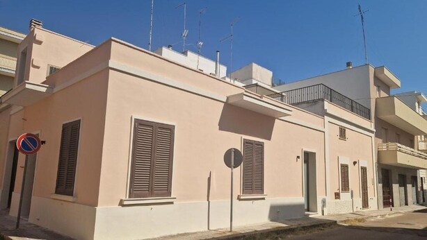 Un edificio de dos pisos con techo plano y un balcón en el nivel superior, con un cartel de no estacionamiento en la calle.